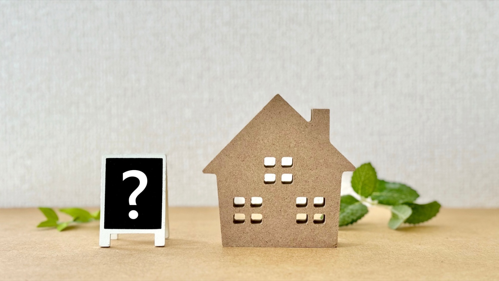 木製の家型オブジェと「？」マークの看板。住宅購入や不動産に関する疑問や悩みを象徴するイメージ。