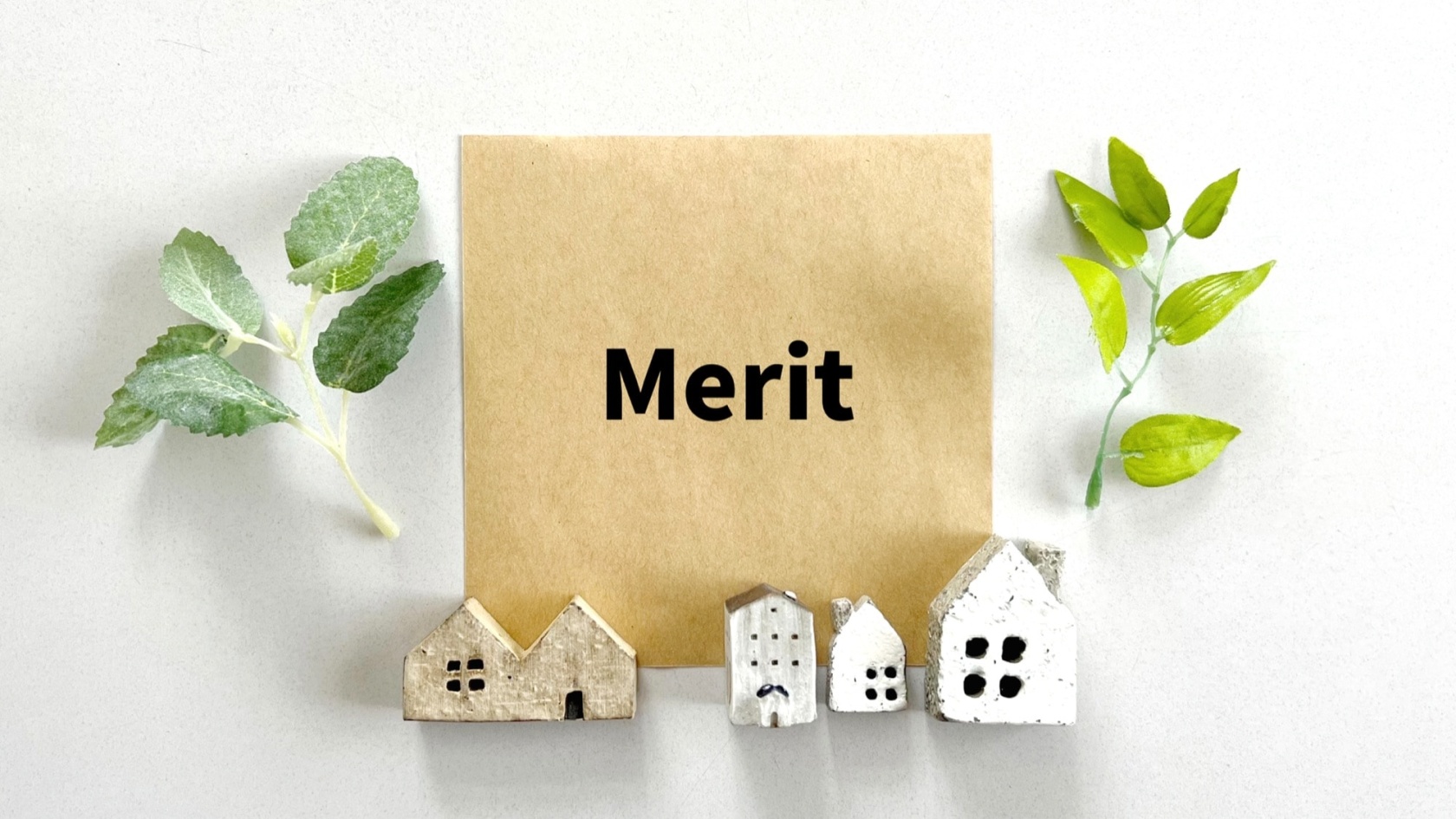 「Merit」と書かれた茶色の紙を中心に、複数のミニチュアの家と緑の葉が配置されたイメージ。住まいや不動産に関するメリット、価値、利点を象徴する。